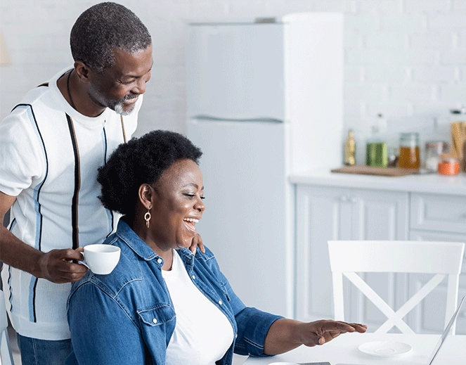 african american couple in white kitchen smiling looking at laptop