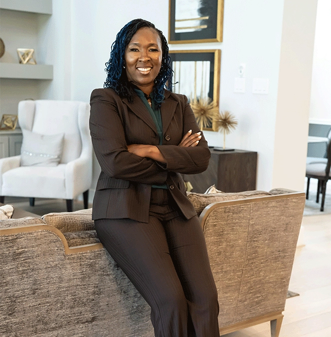 black woman wearing brown suit in living room leaning against couch